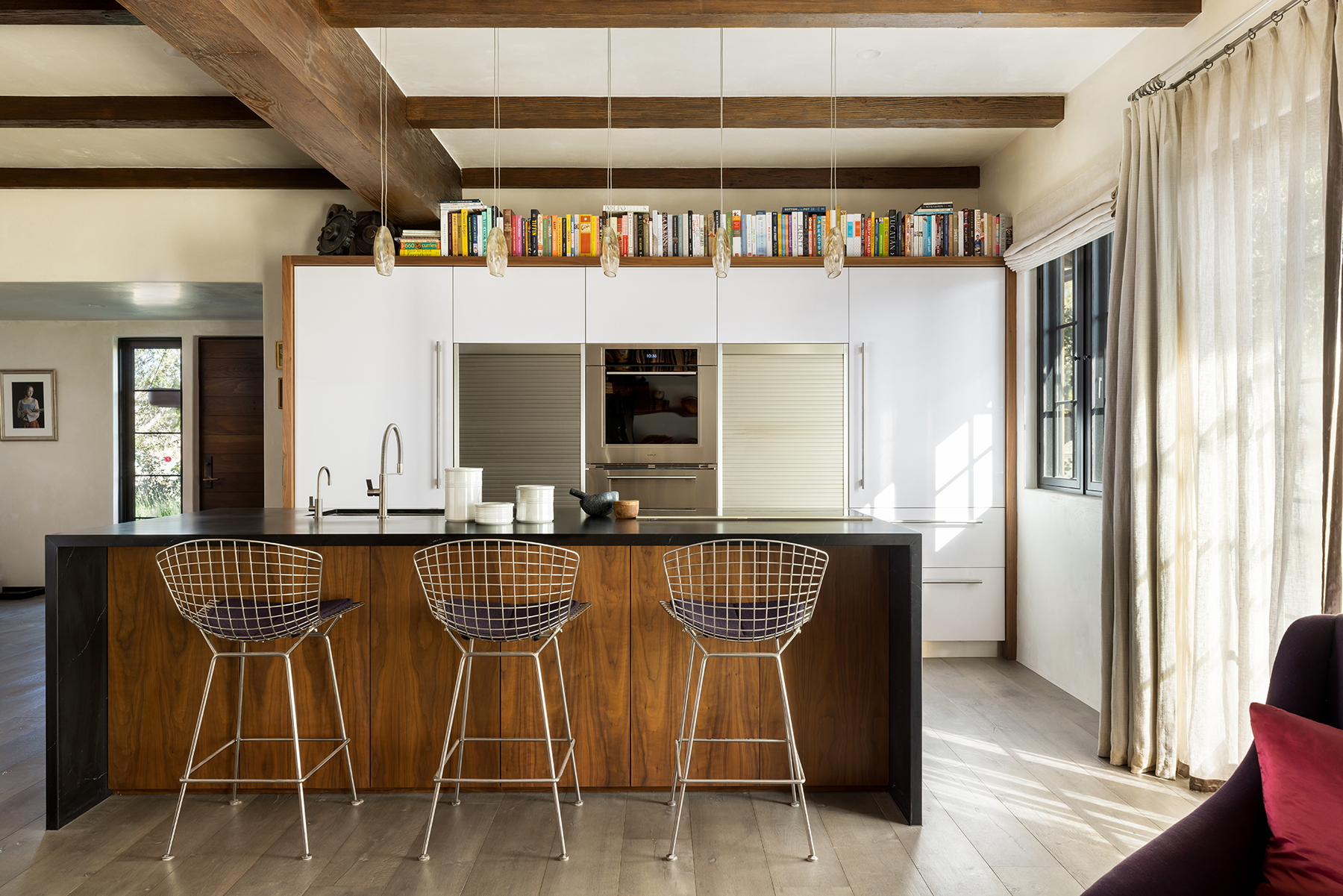 A brightly lit kitchen, with an island and 3 chairs.